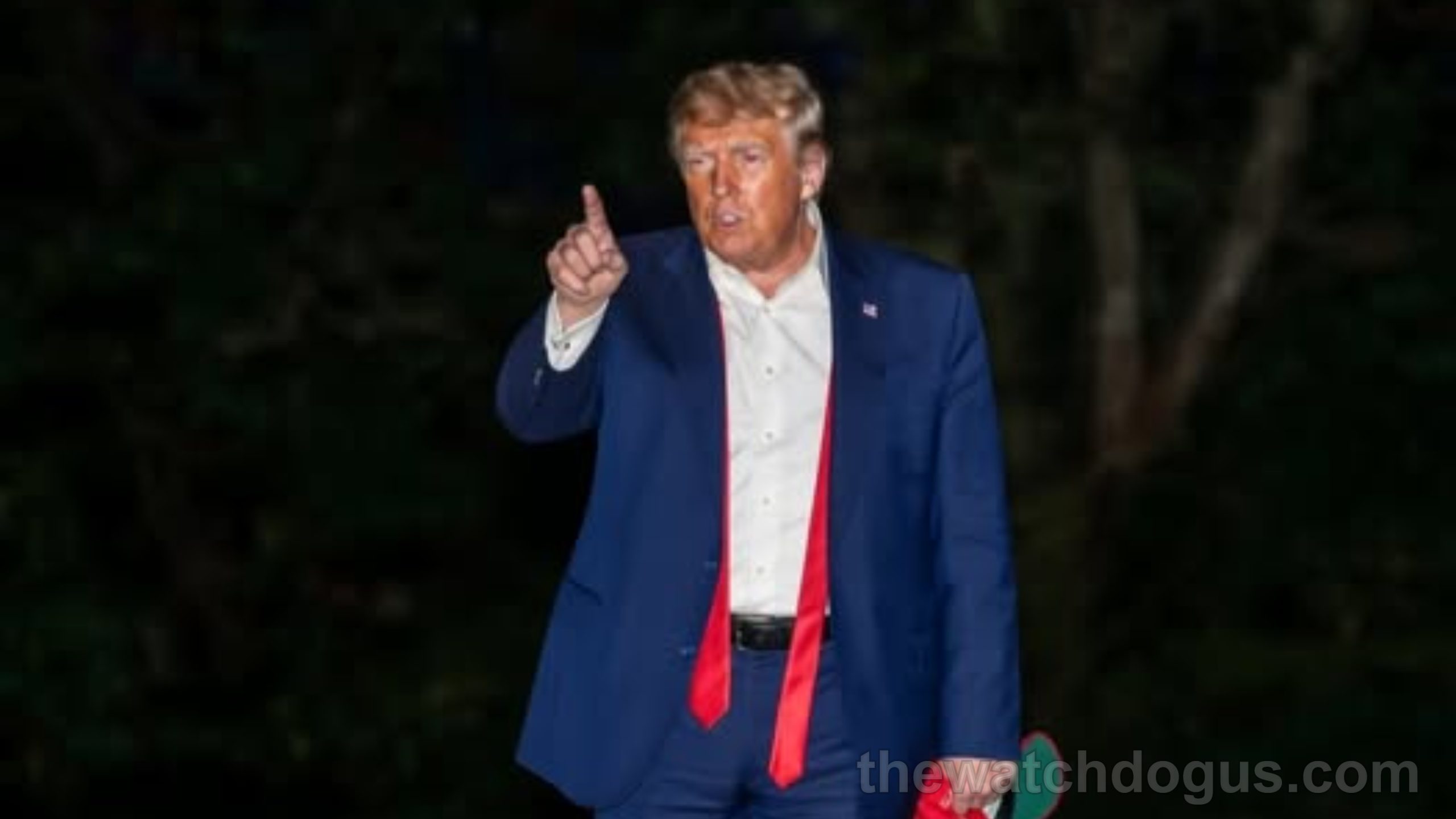 Man in blue suit giving thumbs up while holding mysterious item sighting during evening appearance