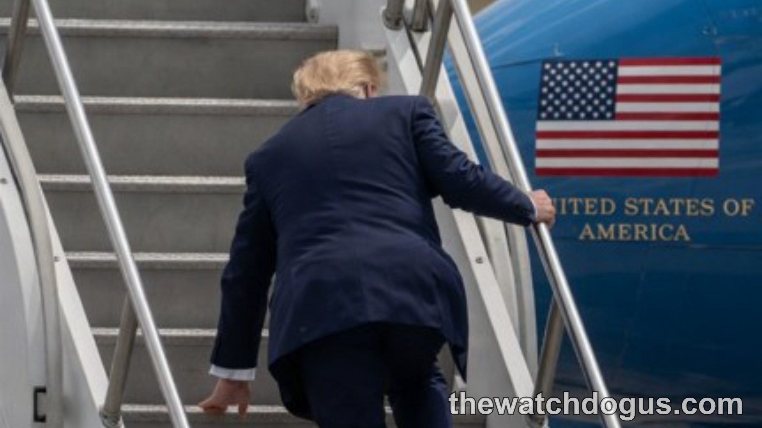 Man in dark suit climbing Air Force One stairs with American flag and United States of America text visible