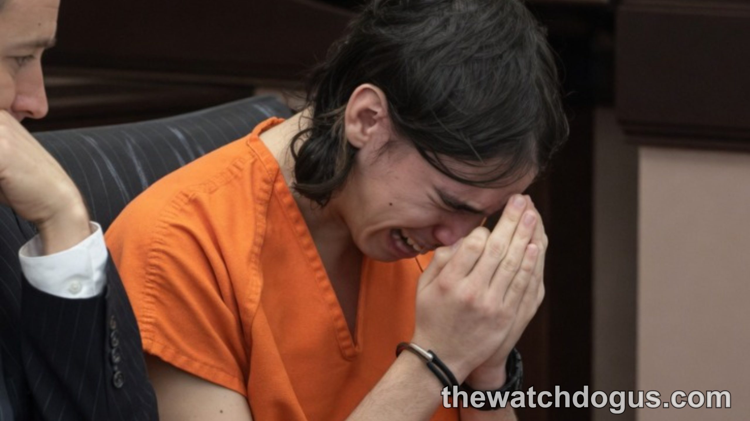 Teen in orange prison jumpsuit appears emotional during court proceeding, seated with attorney in justice system hearing