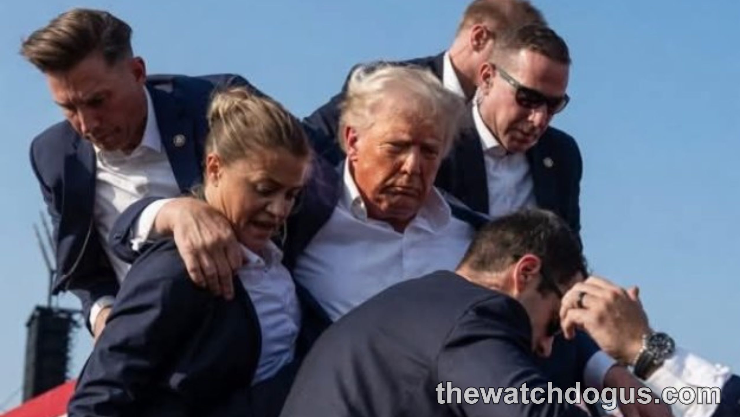 Multiple security personnel assist a man in a light blue shirt during Trump shooting incident at campaign event