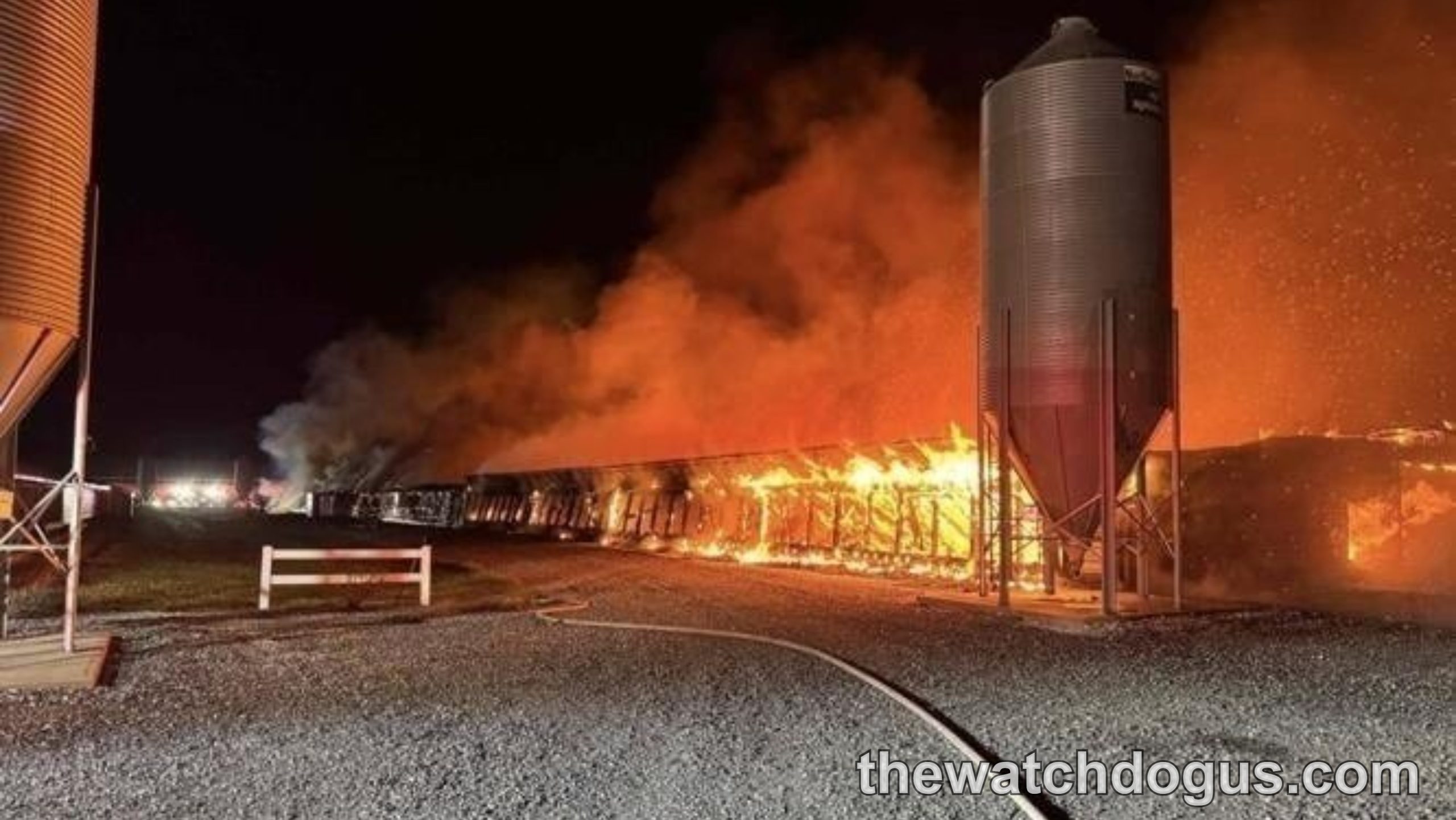Nighttime hillside fire damage at agricultural facility with burning structures and metal grain storage tank