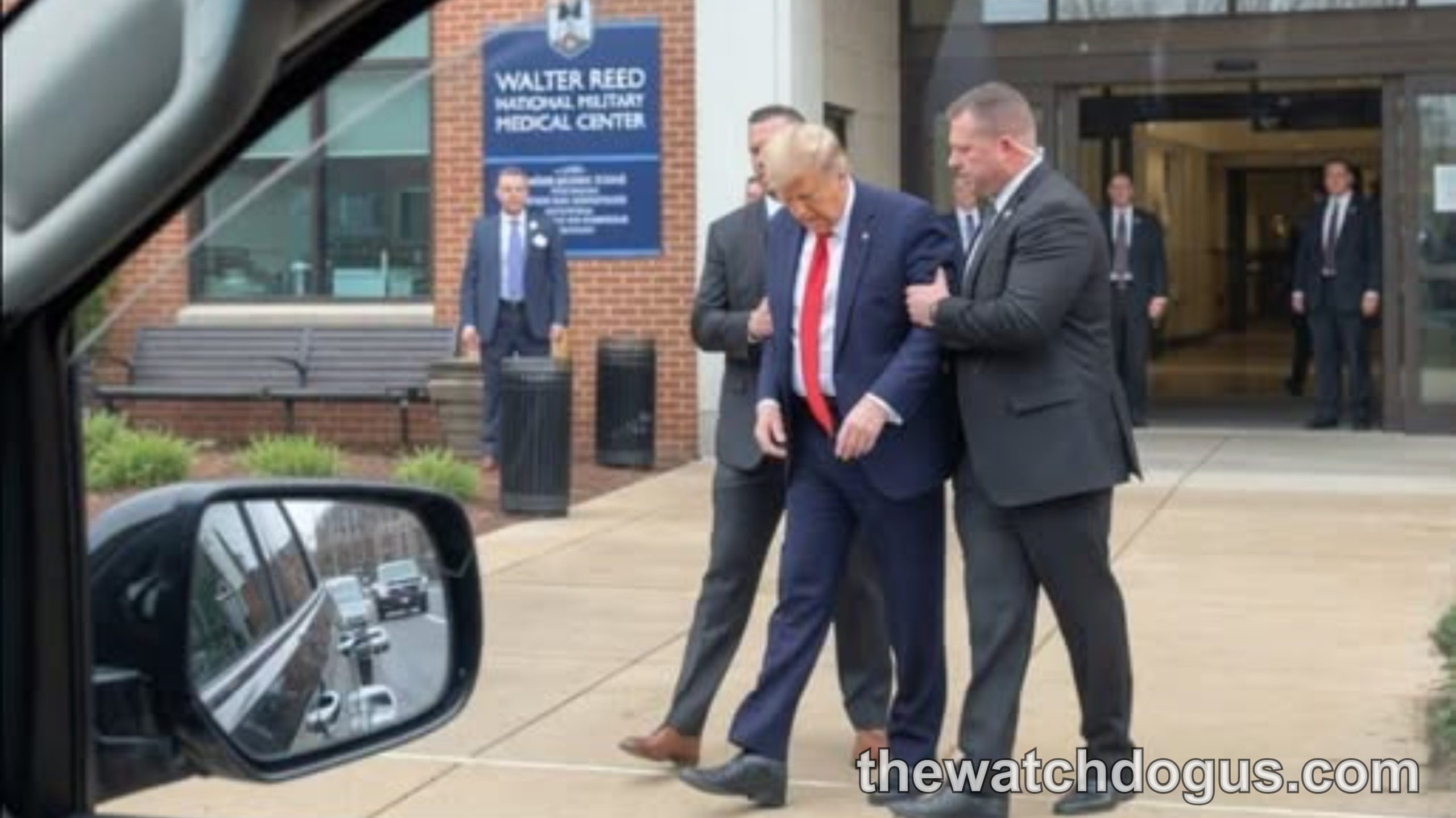 Officials escort man in dark suit and red tie outside Walter Reed Medical Center during Trump health reports visit