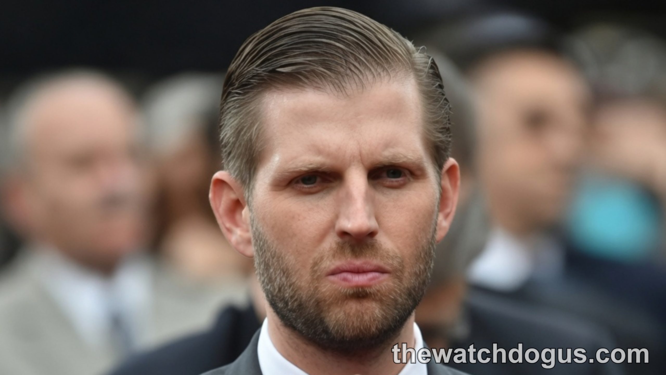 Eric Trump in gray suit and navy tie pointing at camera during public appearance