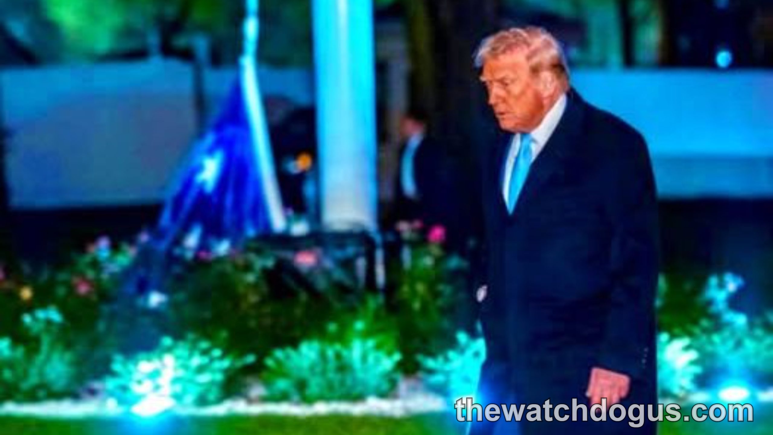 Man in dark suit and overcoat standing on illuminated lawn at night during Trump condition update