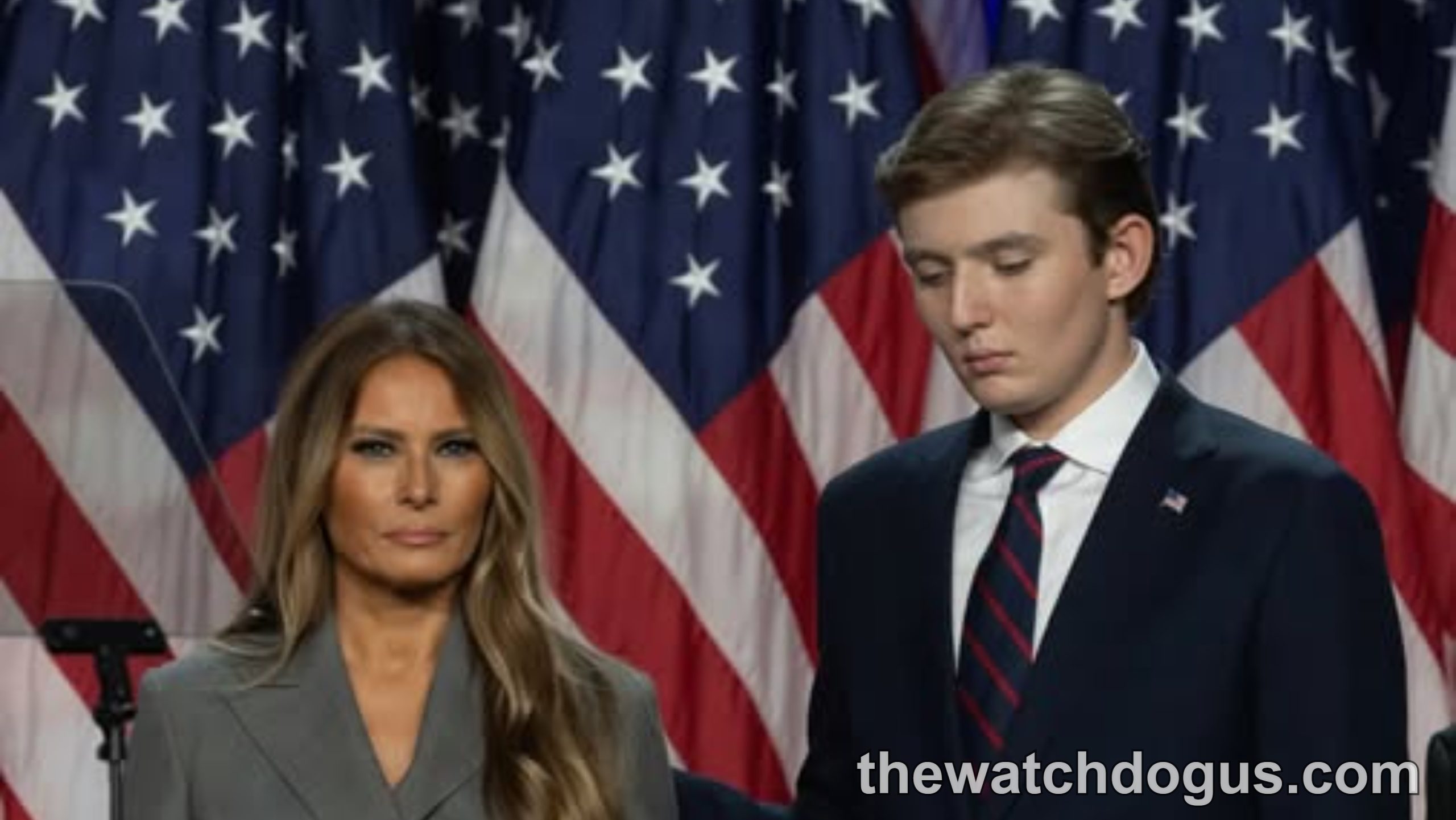 Barron Trump public appearance with woman in gray blazer standing before American flags at formal event