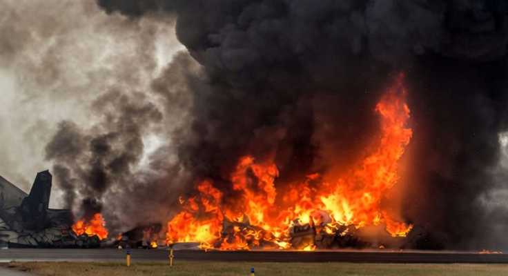 Massive fire and smoke from plane crash wreckage on airport runway with emergency response