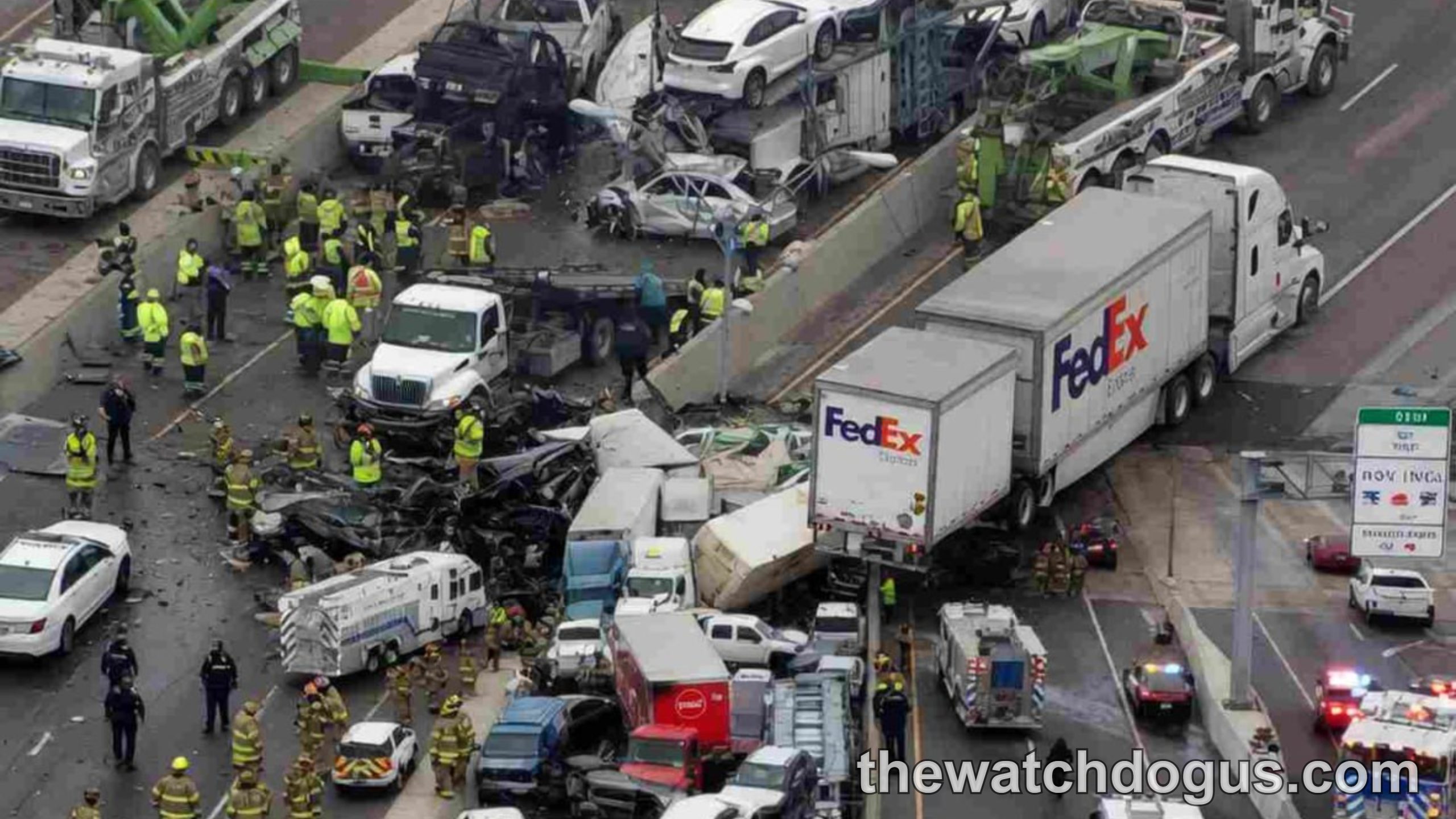 Aerial view of catastrophic disaster on multi-lane highway with dozens of damaged vehicles, emergency responders in yellow vests, and recovery equipment
