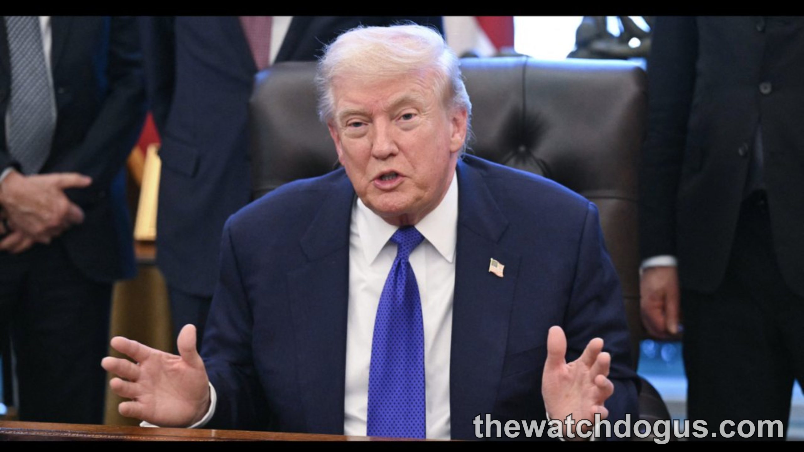 Political figure in formal attire gesturing while speaking at desk with officials present