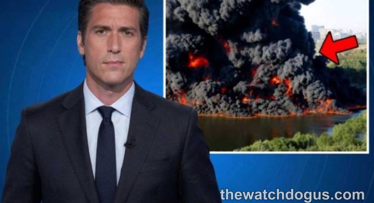 News anchor reporting on national tragedy response with aerial footage of large industrial fire and emergency response