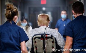 Healthcare workers escort elderly patient in wheelchair during Trump cognitive assessment evaluation at medical facility