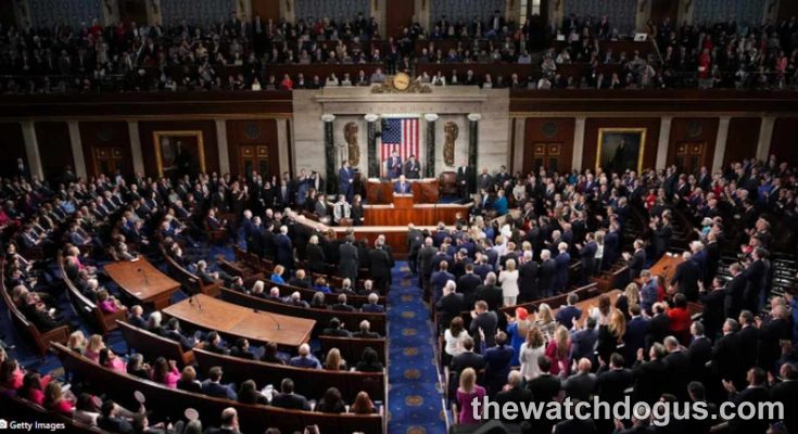 House floor during debate on tax bill with members seated in chamber and American flag backdrop